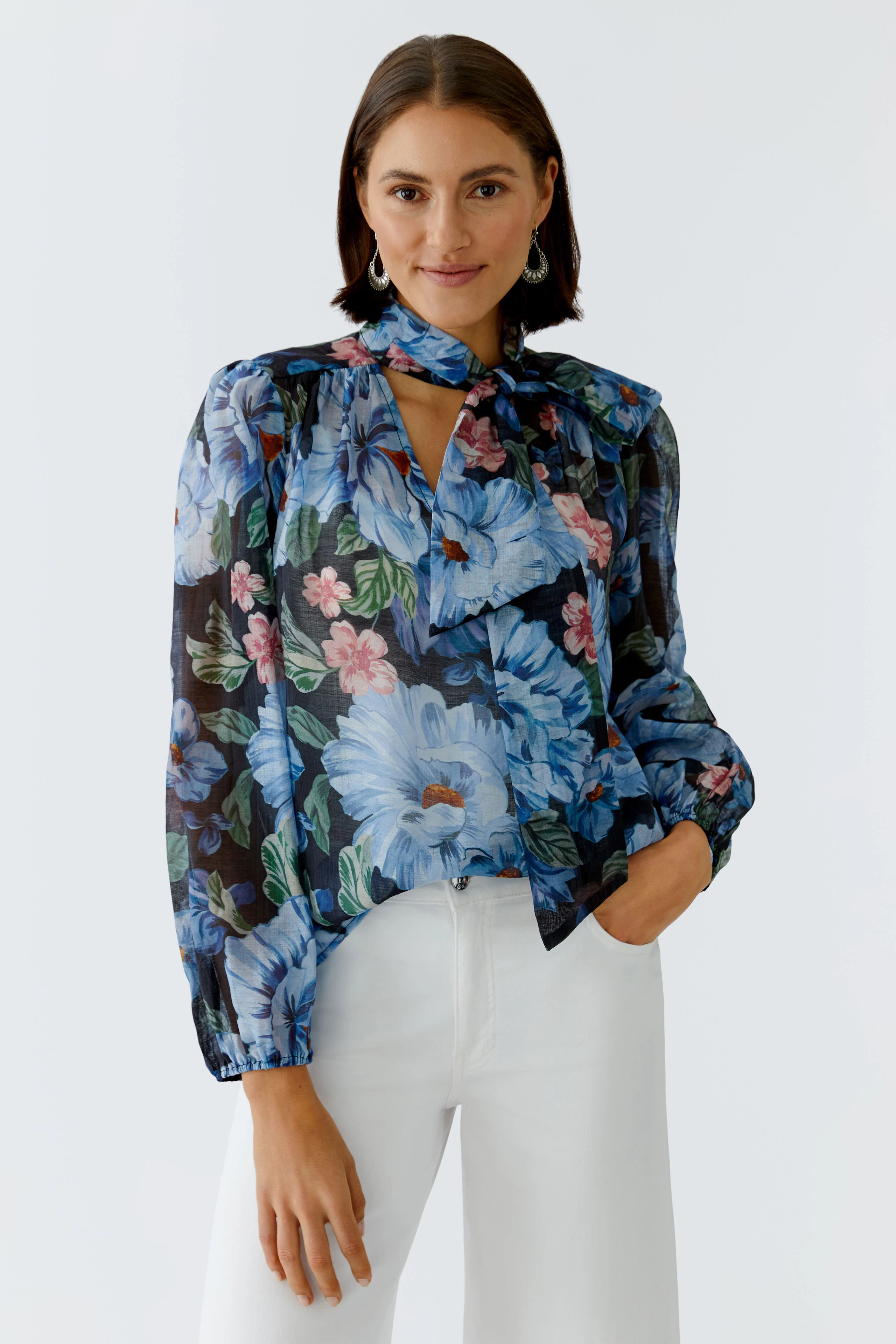 Bluse mit floralem Muster: Frau trägt eine bunte Bluse mit Blumenprint und lässigen weißen Hosen.