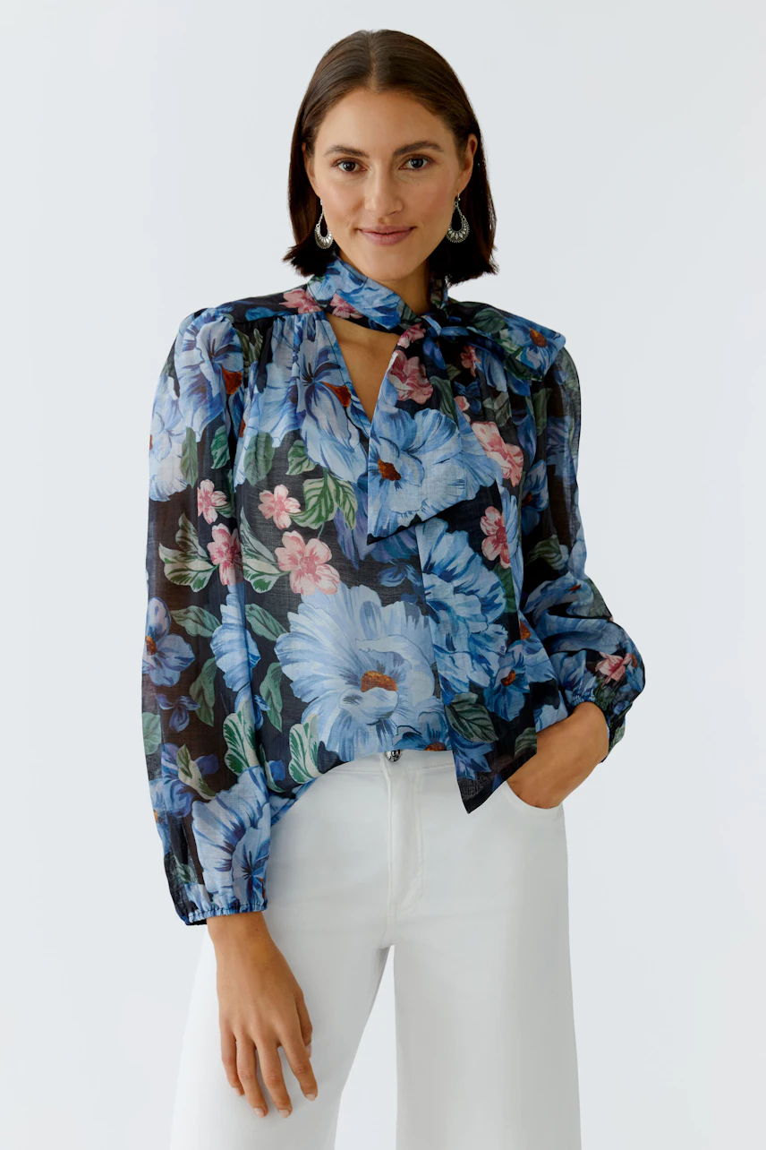 Floral blouse: Woman in a colorful floral blouse with a tie neck and relaxed fit.