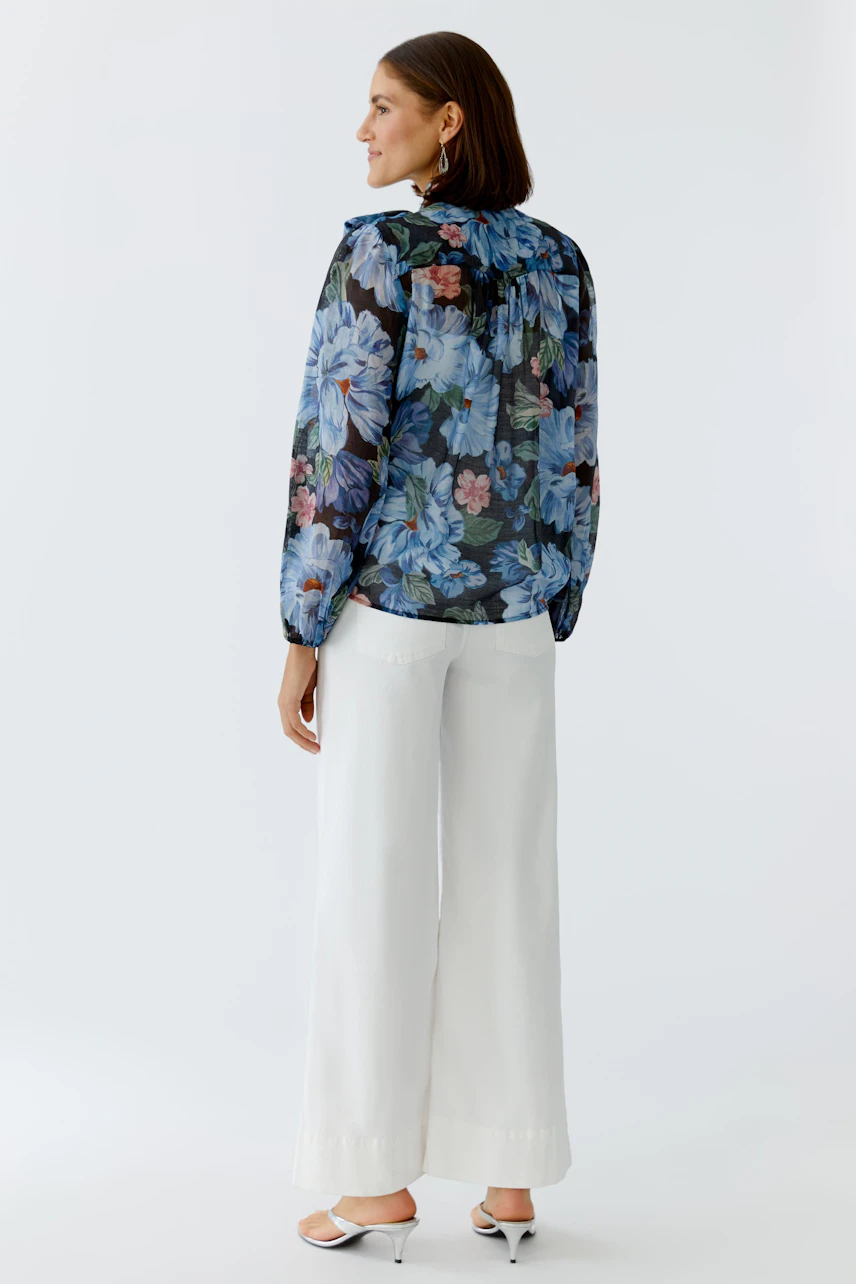 Floral blouse: Woman in a sheer floral blouse with long sleeves and relaxed fit, paired with wide trousers.