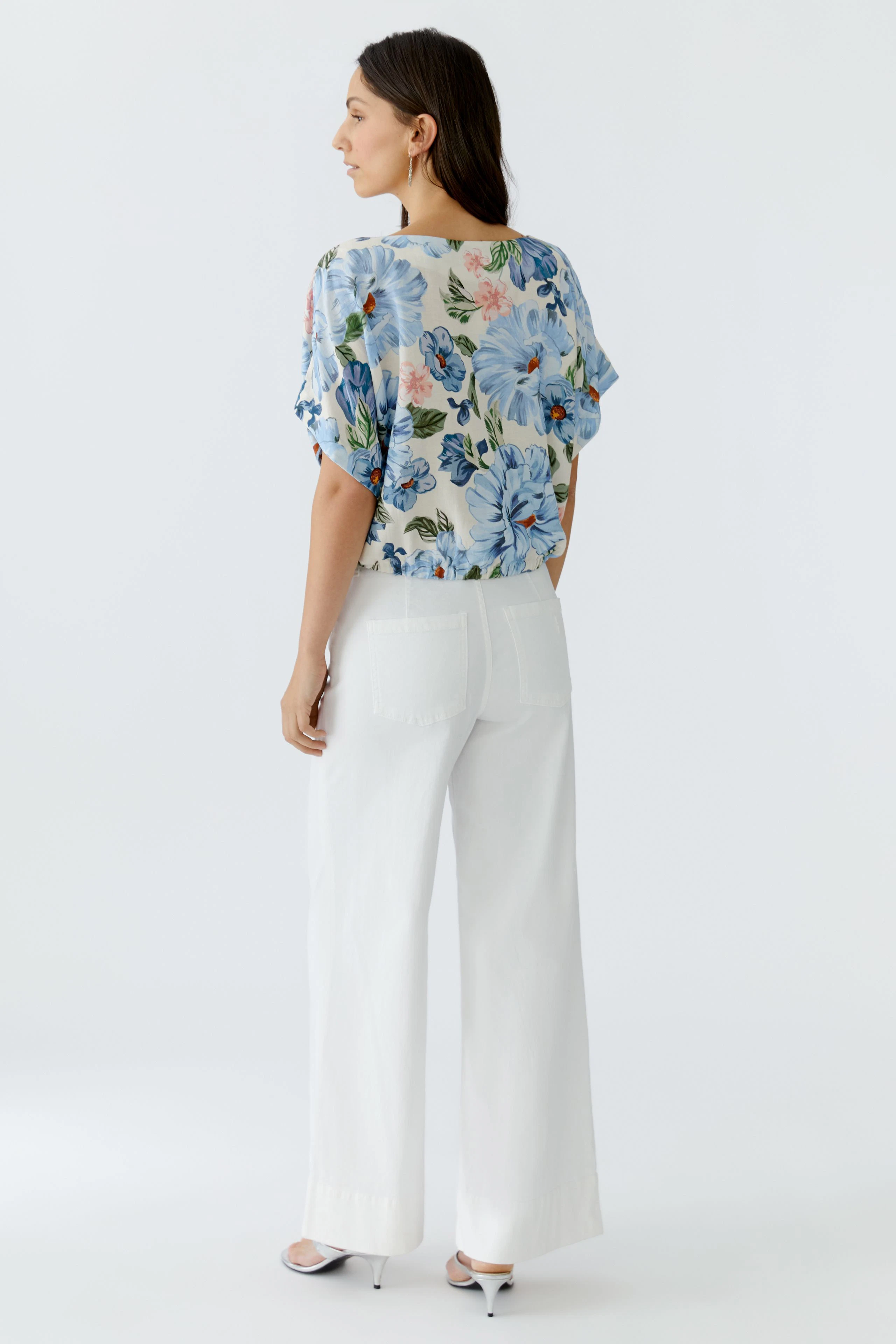Floral blouse: Woman in a loose-fitting blouse with colorful flowers, paired with wide white pants.