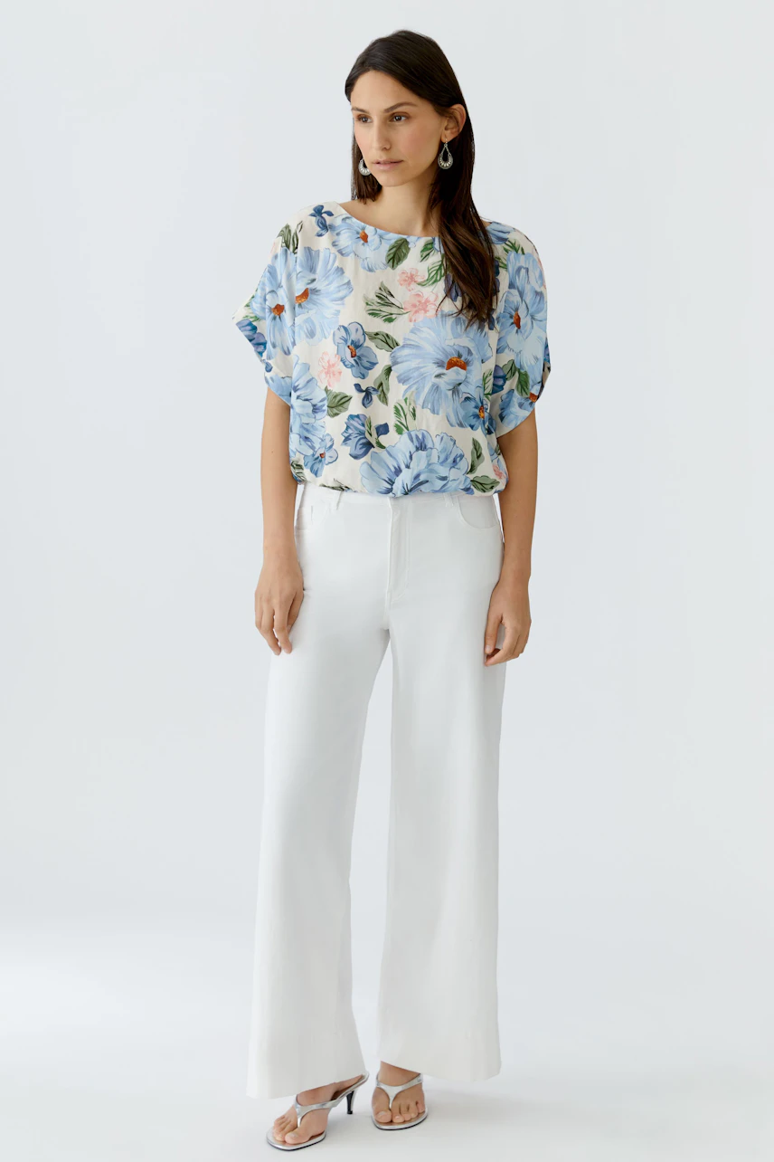 Casual women's blouse: A woman in a floral top paired with white wide-leg pants stands confidently.