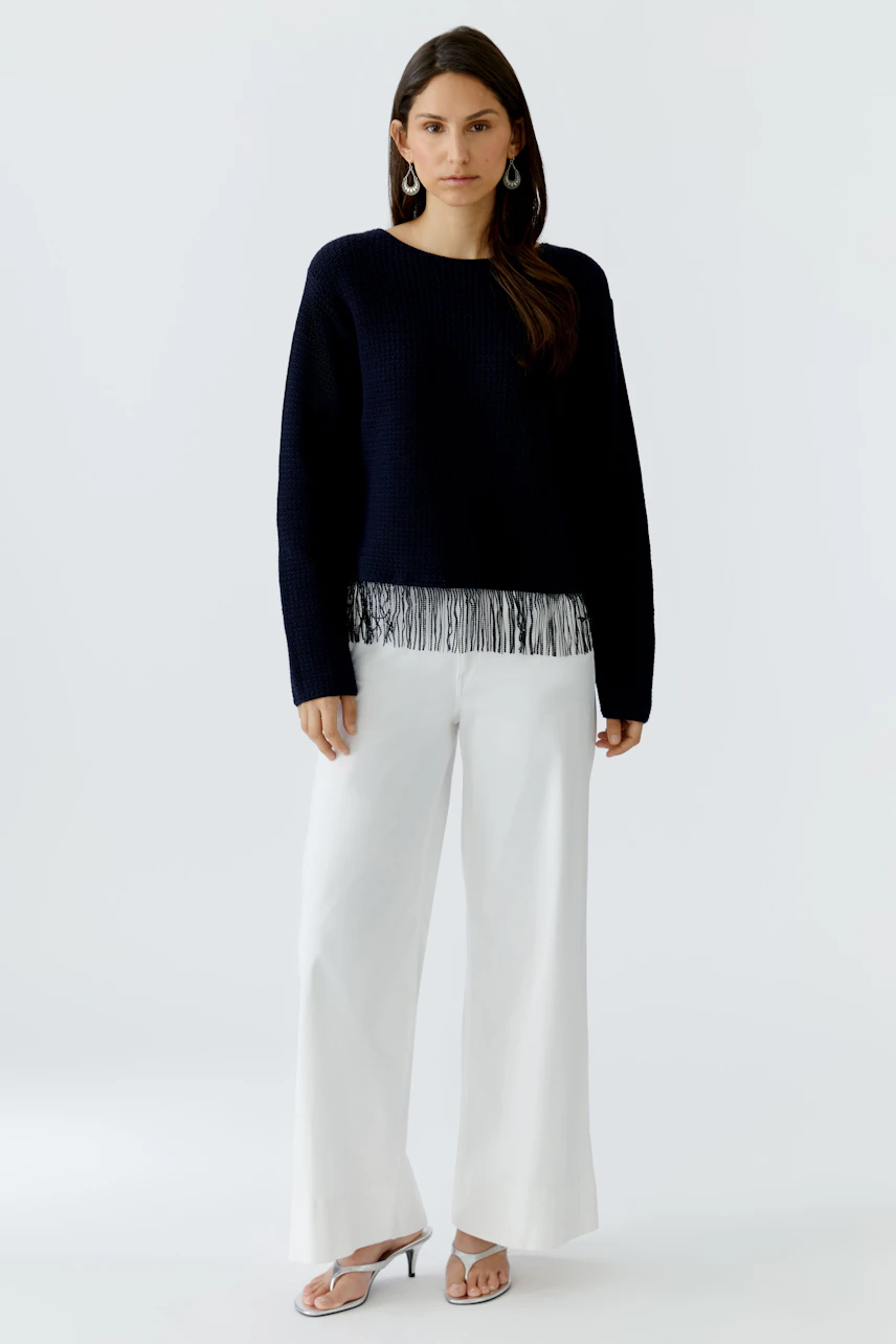 Casual women's pullover: A woman in a navy pullover with fringe detail, paired with white wide-leg pants.