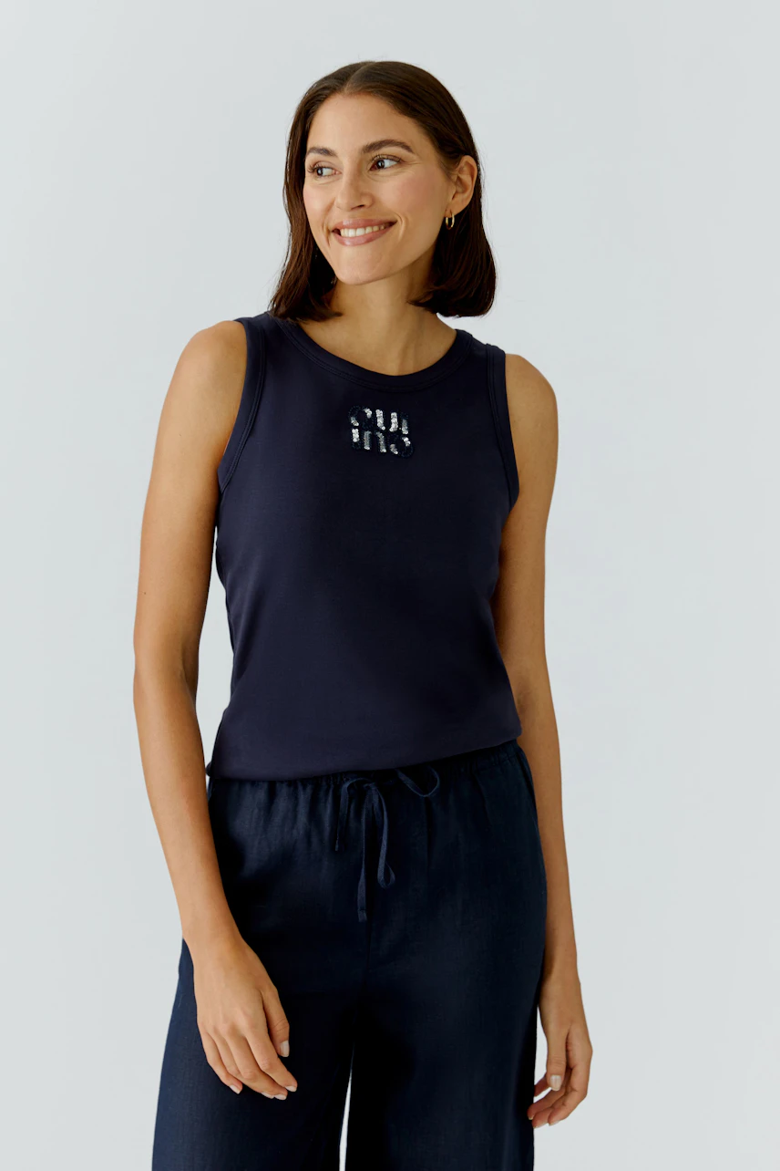 Casual women's tank top: Smiling woman in a navy tank top with a graphic design, paired with relaxed pants.