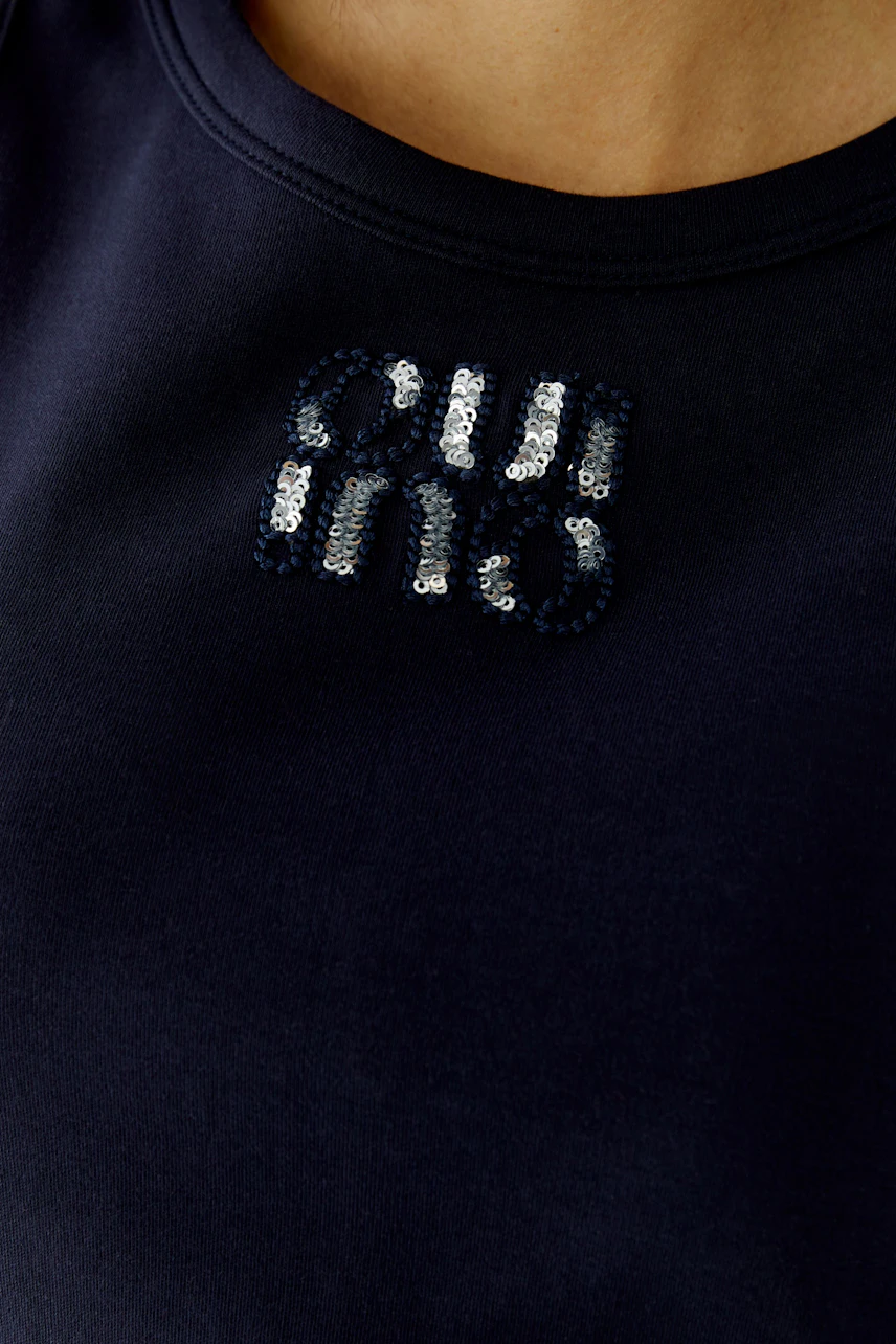 Casual women's tank top: Close-up of a woman wearing a navy top with sequined logo detail.
