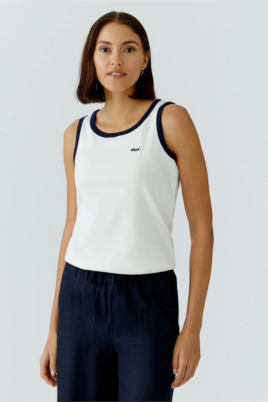 Casual women's tank top: A woman in a white tank top with navy trim, paired with relaxed pants.