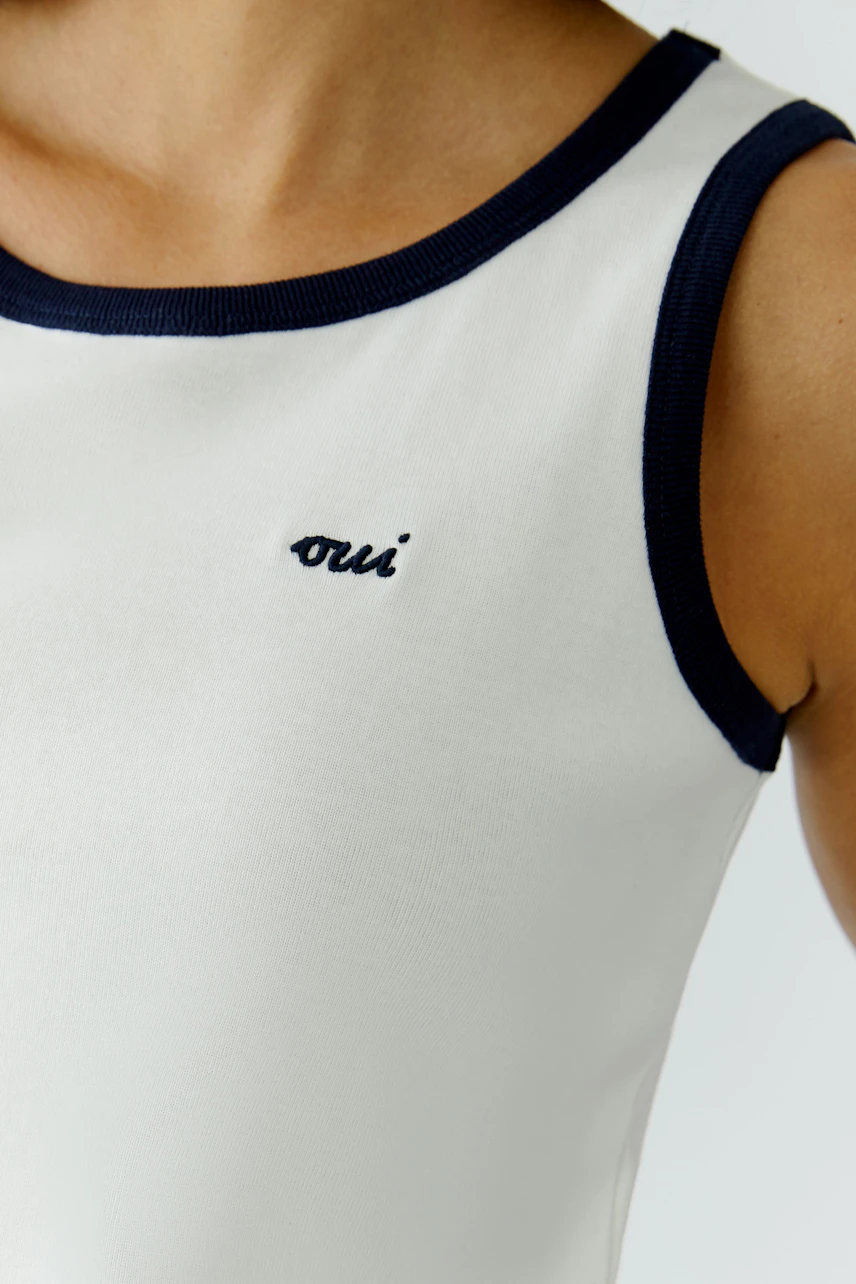 Casual women's tank top: Close-up of a woman wearing a white tank top with navy trim and logo.