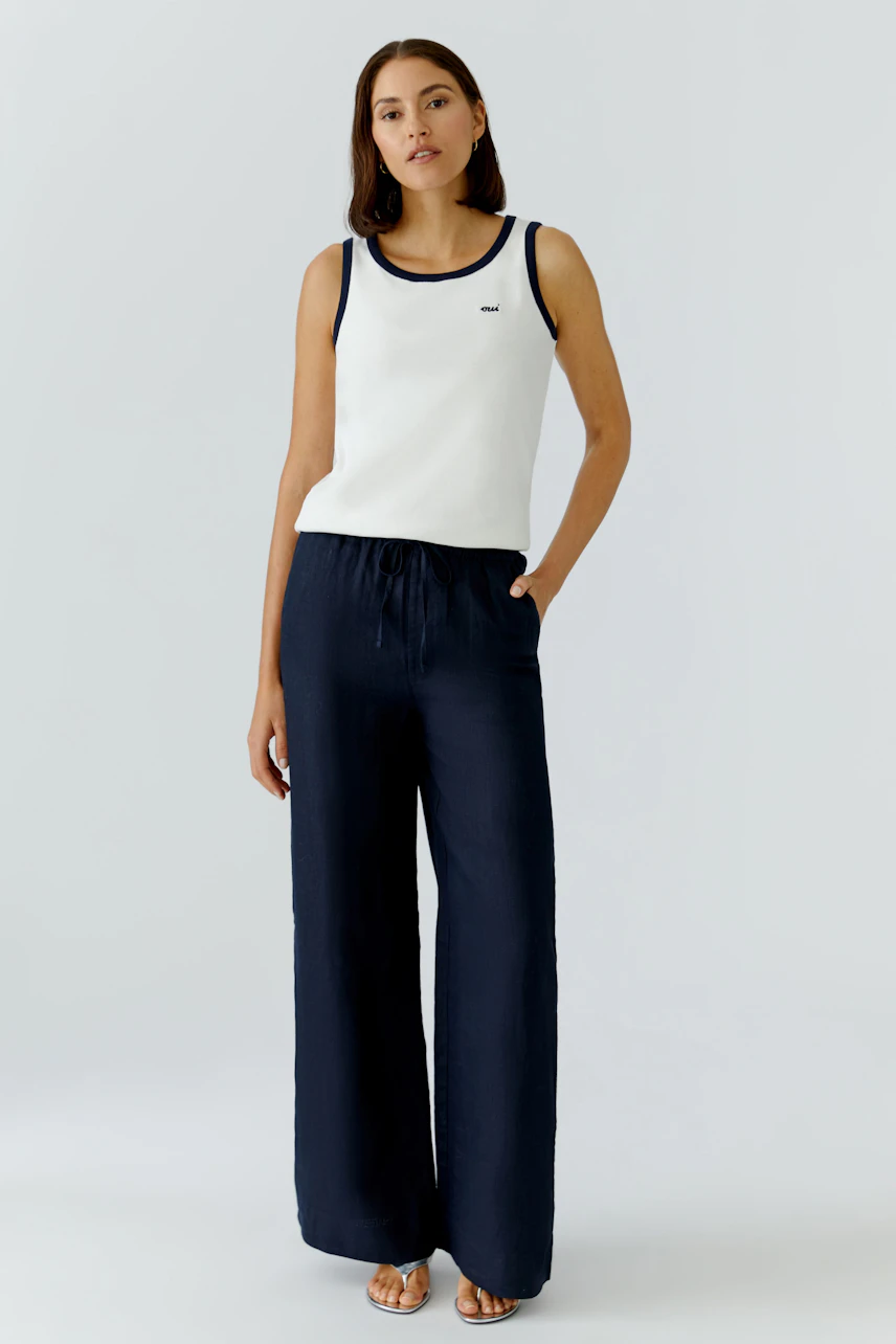 Casual women's tank top: A woman in a white tank top with navy trim and relaxed-fit pants.