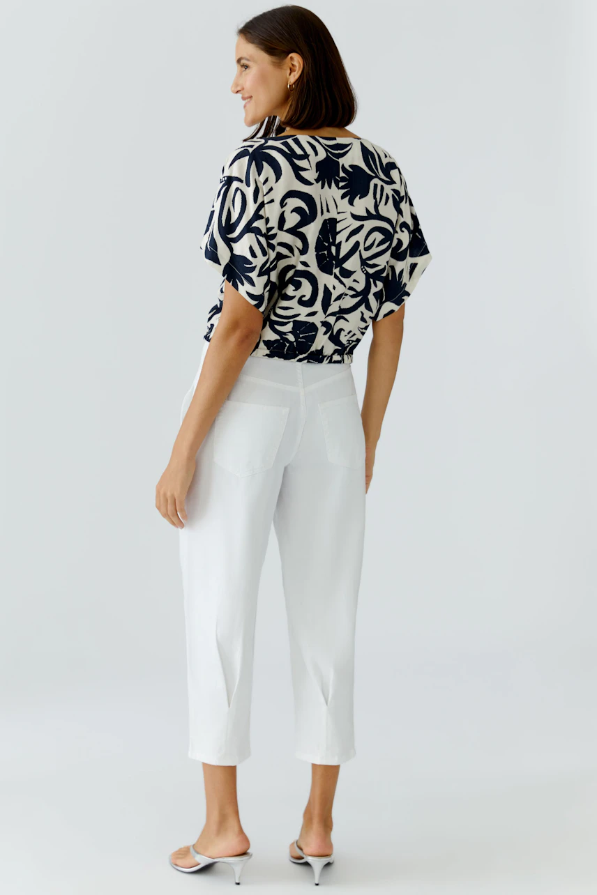 Casual women's blouse: A woman in a patterned blouse paired with white pants, showcasing a relaxed style.