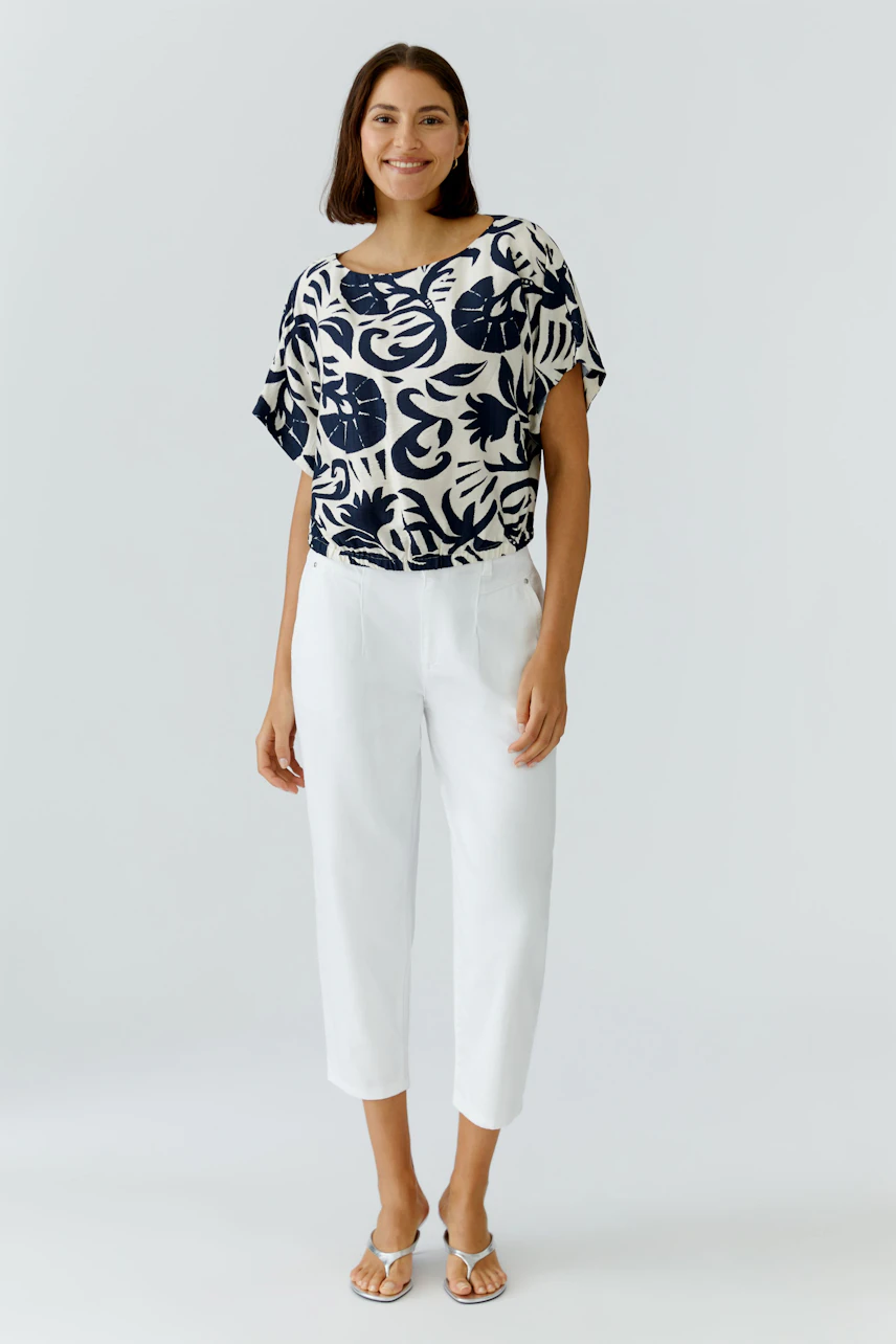Casual women's blouse: A woman in a navy and white floral print blouse paired with white pants.