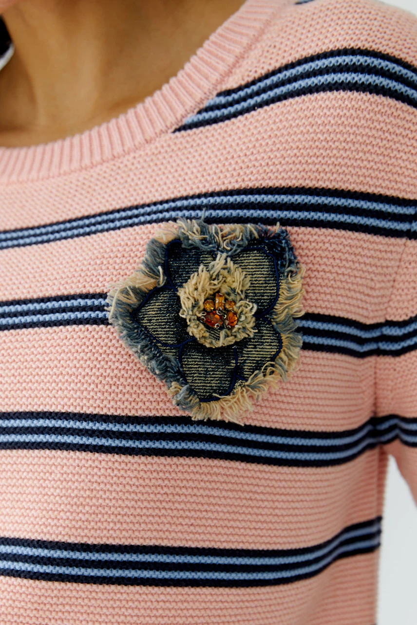 Casual women's pullover: Close-up of a pink striped pullover with a denim flower detail.