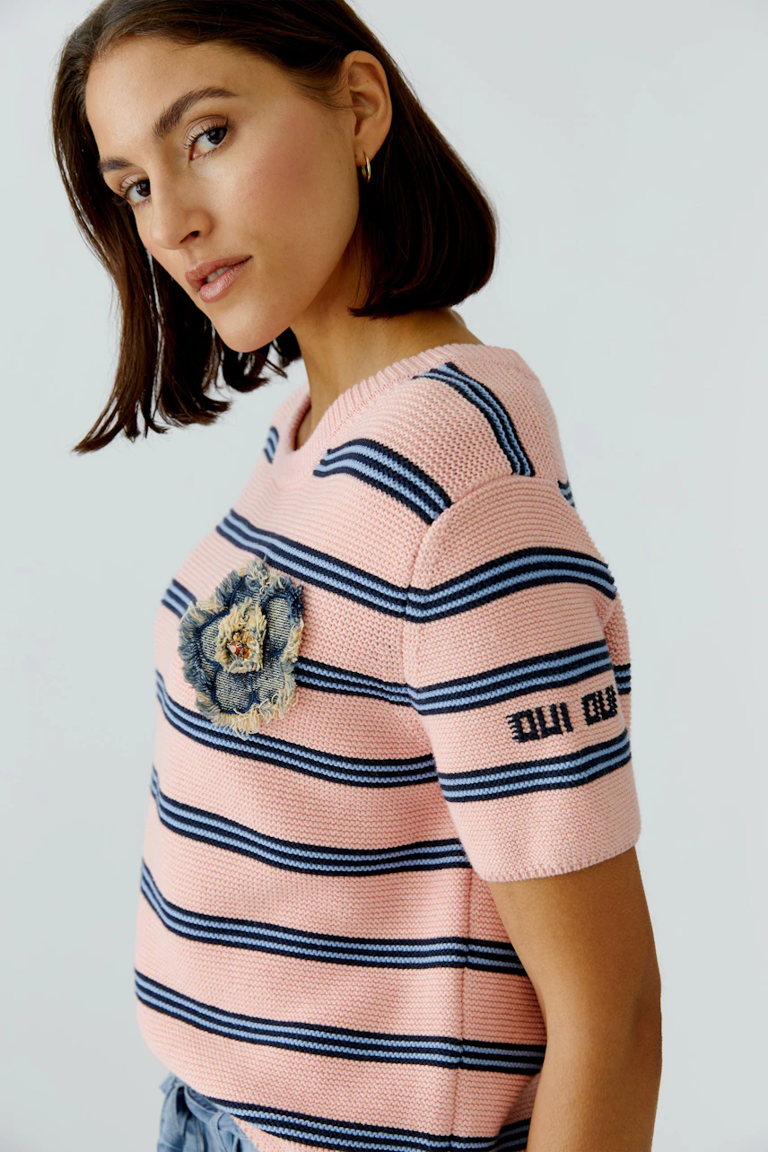 Casual women's pullover: Young woman in a pink striped pullover with floral detail and short sleeves.