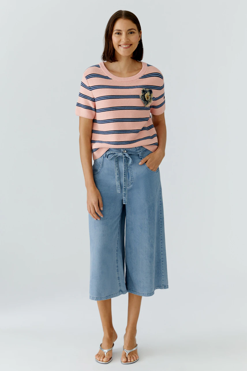 Casual women's pullover: A woman in a pink striped pullover with a pocket and relaxed-fit denim culottes.