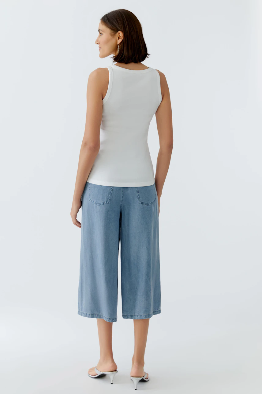 Casual women's tank top: A woman in a white tank top and light blue culottes stands confidently.