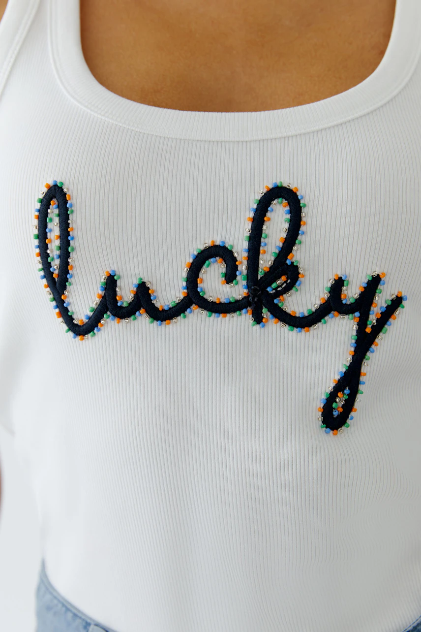 Casual women's tank top: Close-up of a woman wearing a white top with colorful 'lucky' embroidery.