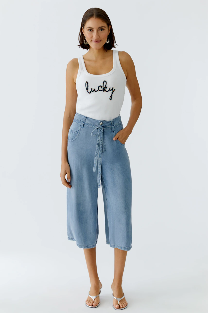 Casual women's tank top: Woman in a white tank top with 'lucky' print, paired with light blue culottes.