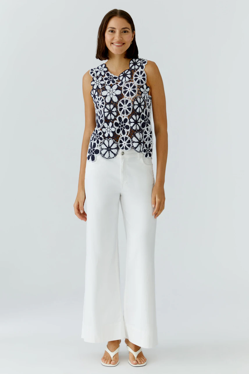 Casual women's top: Young woman in a sleeveless, floral-patterned top paired with wide white pants.