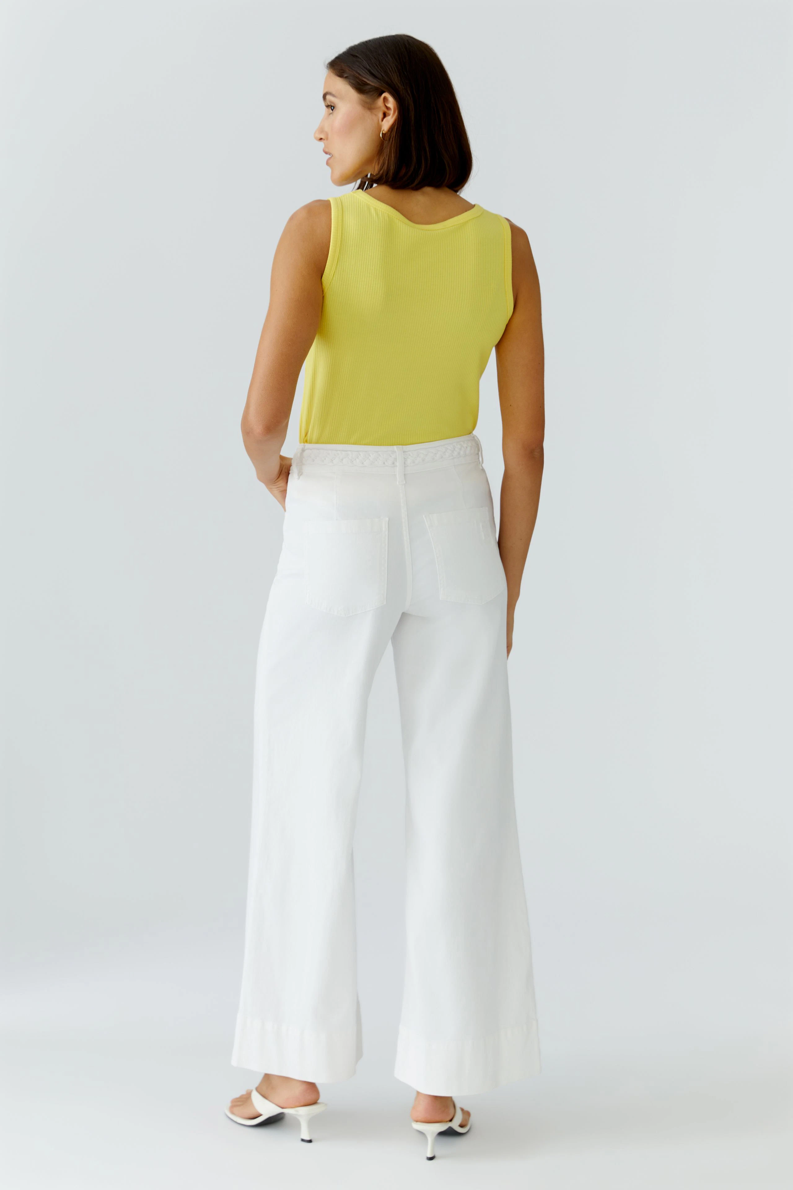 Casual women's top: Woman in a yellow sleeveless top and white wide-leg pants, viewed from the back.