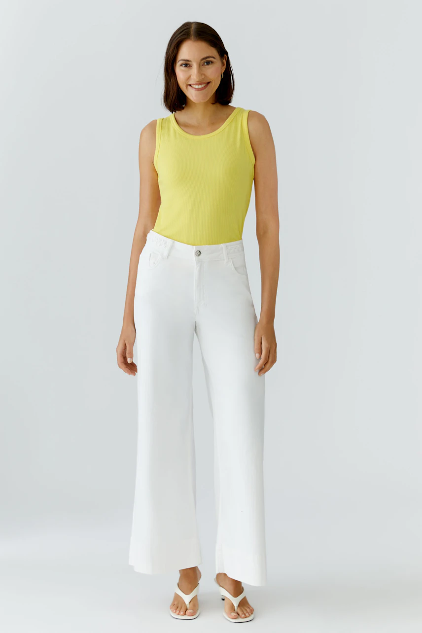 Casual women's top: Woman in a yellow sleeveless top with white wide-leg pants and sandals, smiling.
