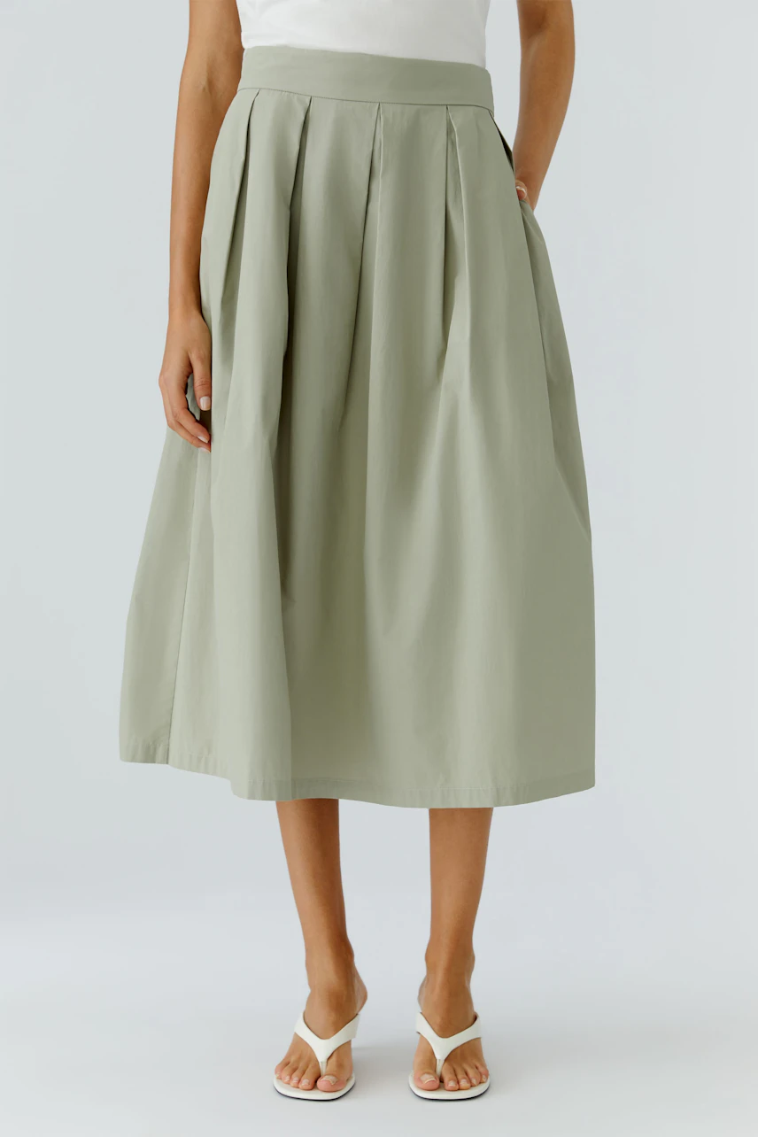A-line skirt: Woman in a light green A-line skirt with a white top and sandals, standing gracefully.