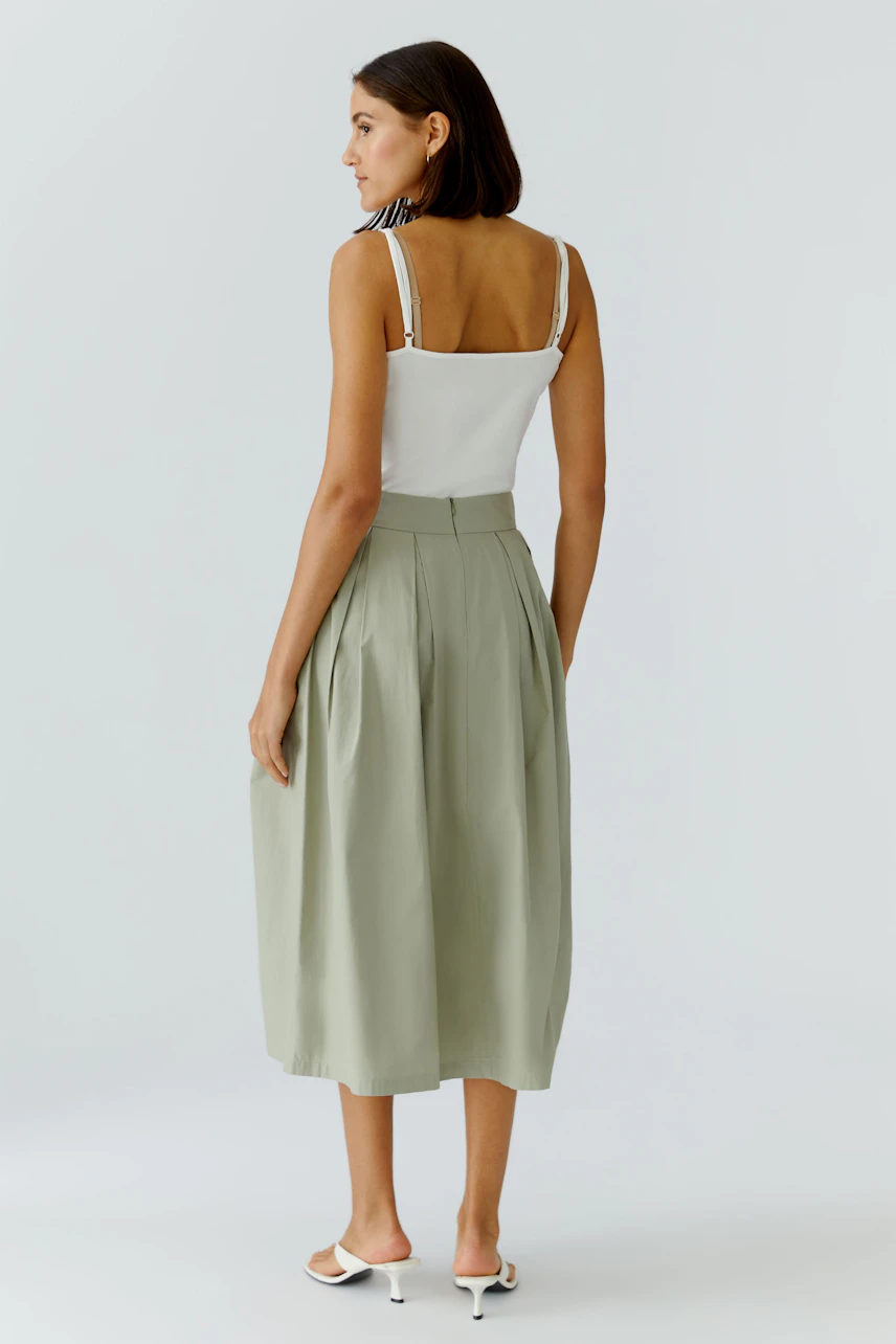 Woman in a white top and green A-line skirt, standing confidently. Casual and stylish look.