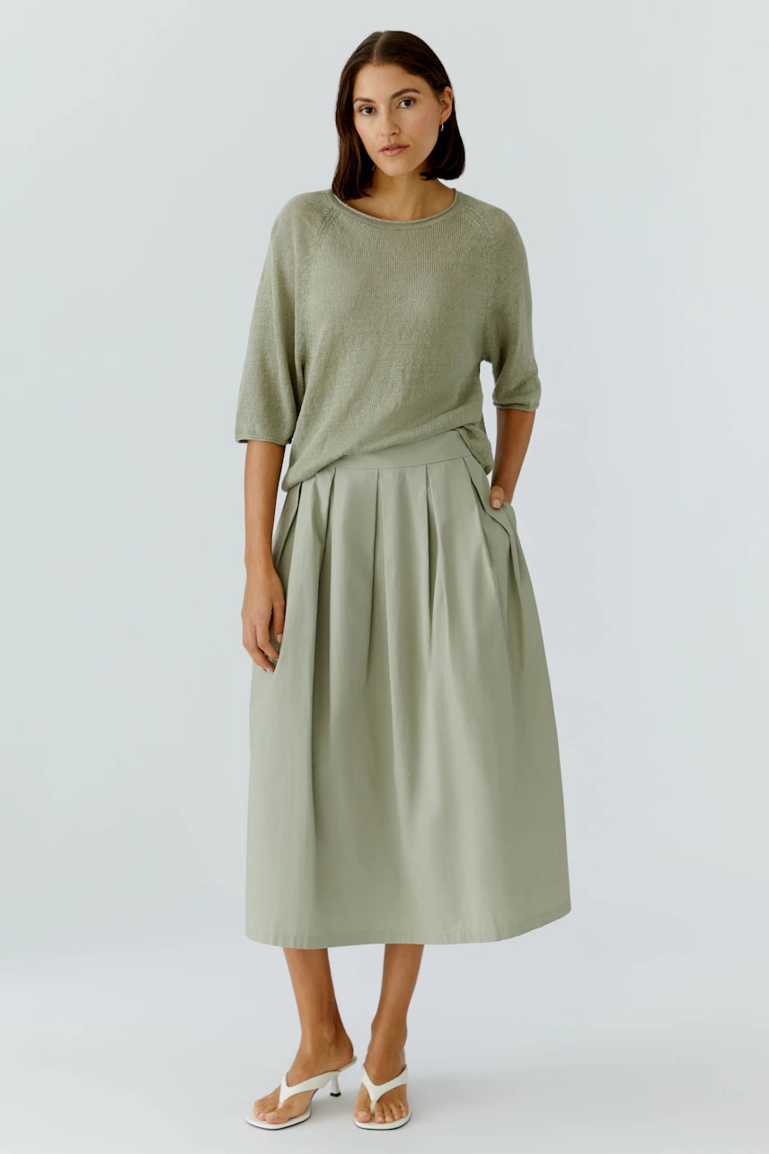 Woman in A-line skirt: Casual look with a light green top and sandals, standing confidently.