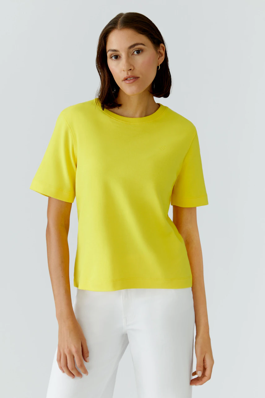 Casual women's T-shirt: Woman in a bright yellow T-shirt and white pants, standing confidently.