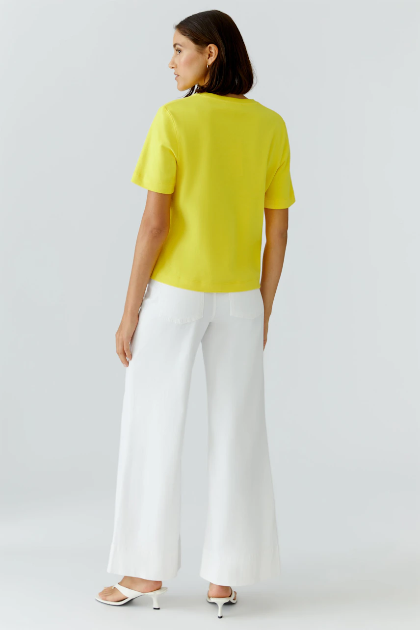Casual women's T-shirt: Woman in a bright yellow T-shirt and white pants, viewed from the back.
