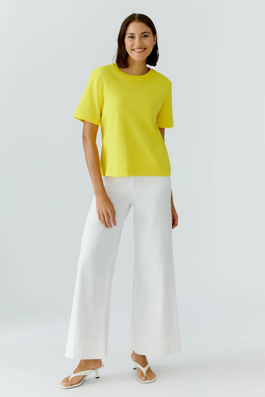 Casual women's T-shirt: Woman in a bright yellow T-shirt and white wide-leg pants, smiling confidently.