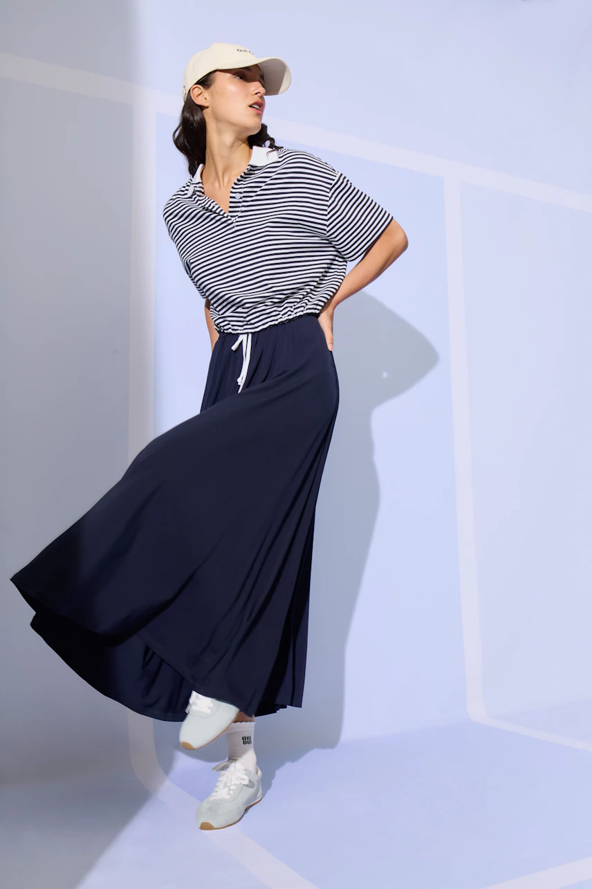 Woman in striped top and navy A-line skirt, wearing a cap and sneakers, posing confidently.