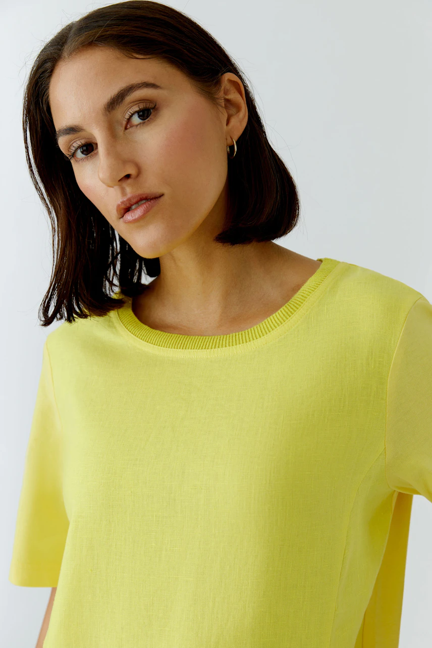 Woman in a bright yellow shift dress, short sleeves, looking confidently.