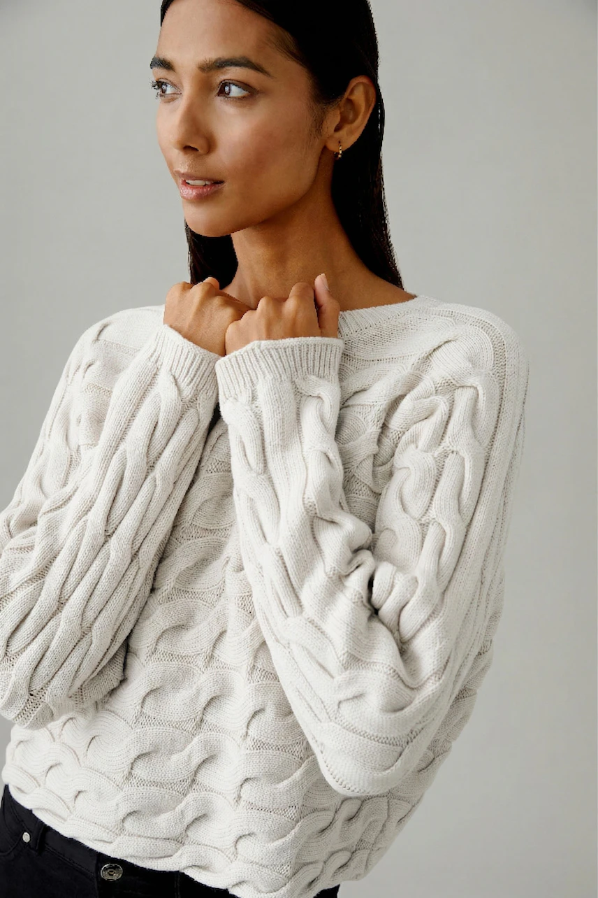 Casual women's pullover: Woman in a cozy, cream cable-knit pullover, looking relaxed.