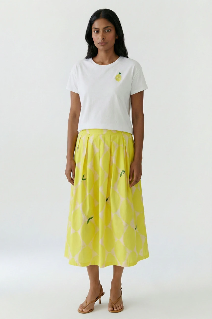 Woman in a white tee and yellow pleated skirt with subtle patterns, standing confidently.