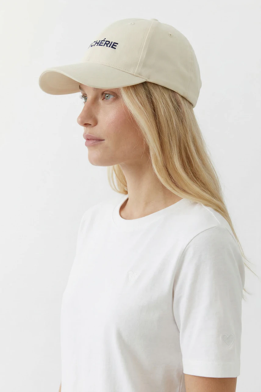 Damen-Hut: Frau mit beigem Hut und weißem T-Shirt blickt zur Seite.