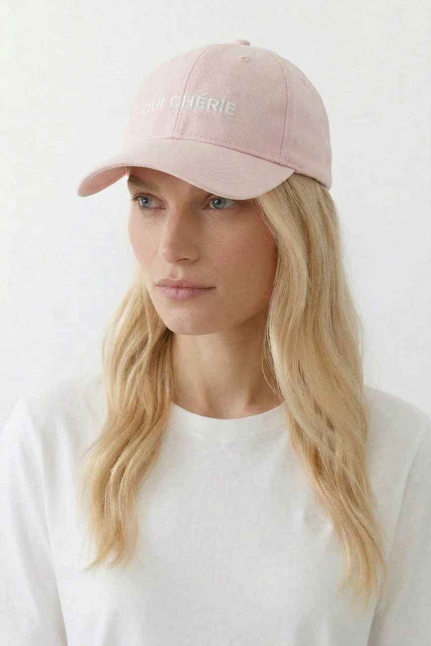 Casual pink hat: Woman in a pink cap with 'Oui Chérie' text, wearing a simple white shirt.