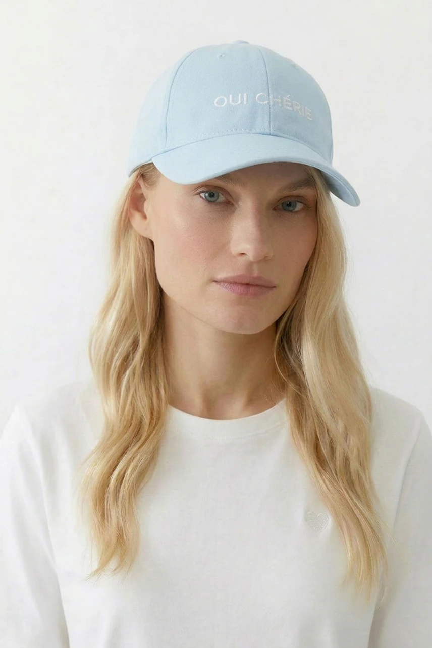 Lässiger Damen-Hut: Frau mit hellblauer Kappe und "Oui Chérie" Schriftzug auf weißem Shirt.
