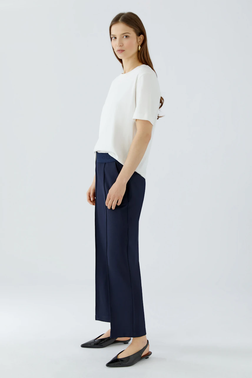 Woman in navy culotte and white top, standing confidently. Simple, modern style with black flats.