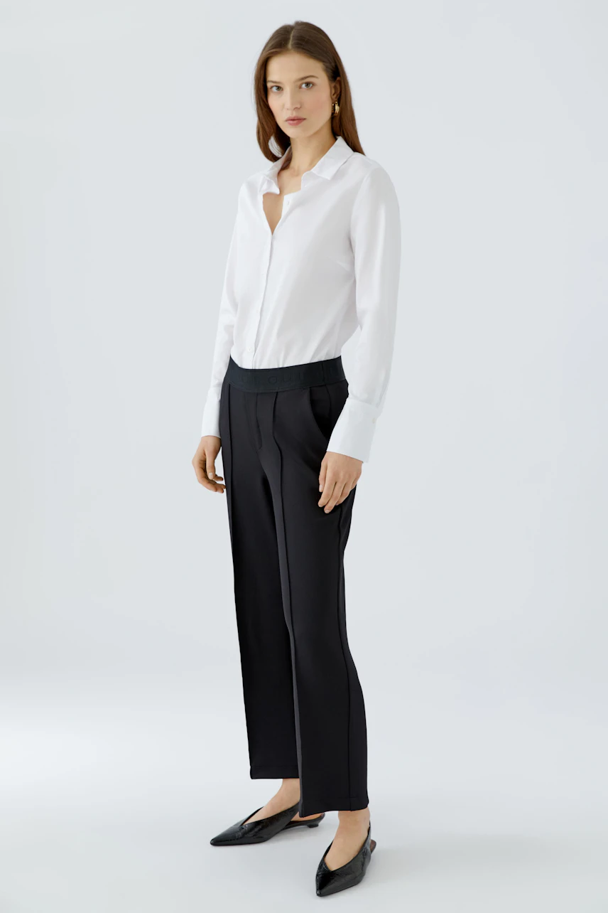 Woman in black culotte pants and white shirt, standing confidently in black flats.