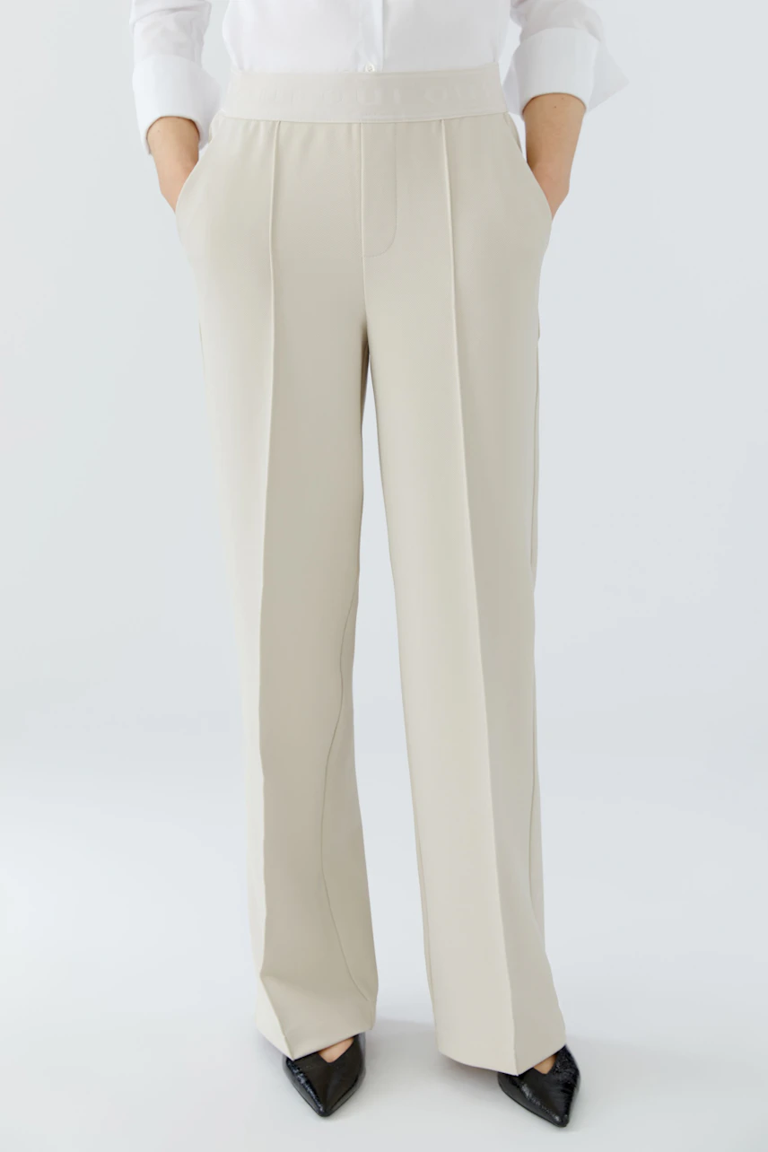Chic women's trousers: A woman in cream-colored trousers with a relaxed fit and side pockets.