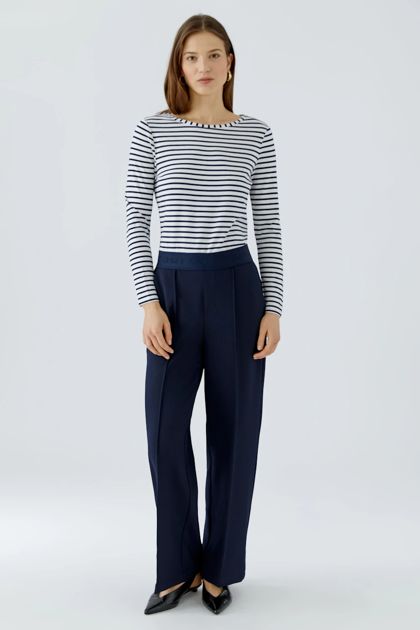 Modern women's trousers: A woman in navy trousers with a relaxed fit and a white shirt stands confidently.