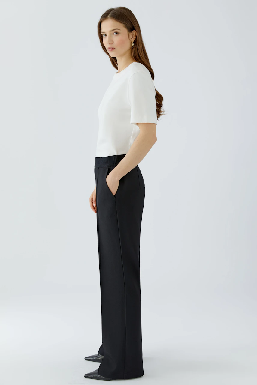 Woman in black pants and white top, side view. Comfortable fit with pockets, ideal for casual wear.