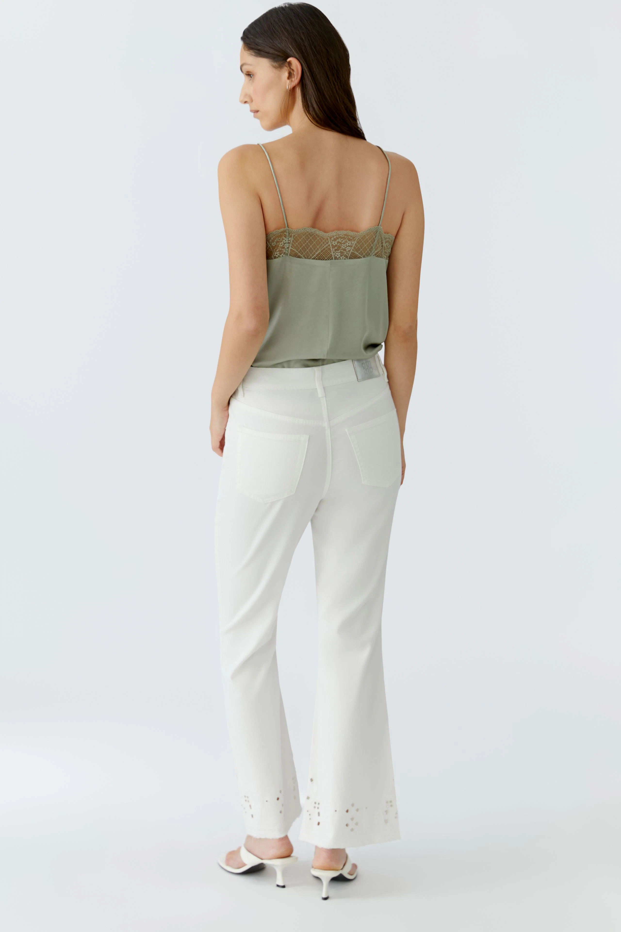 Casual women's top: Woman in a green lace-trimmed top and white pants, viewed from the back.