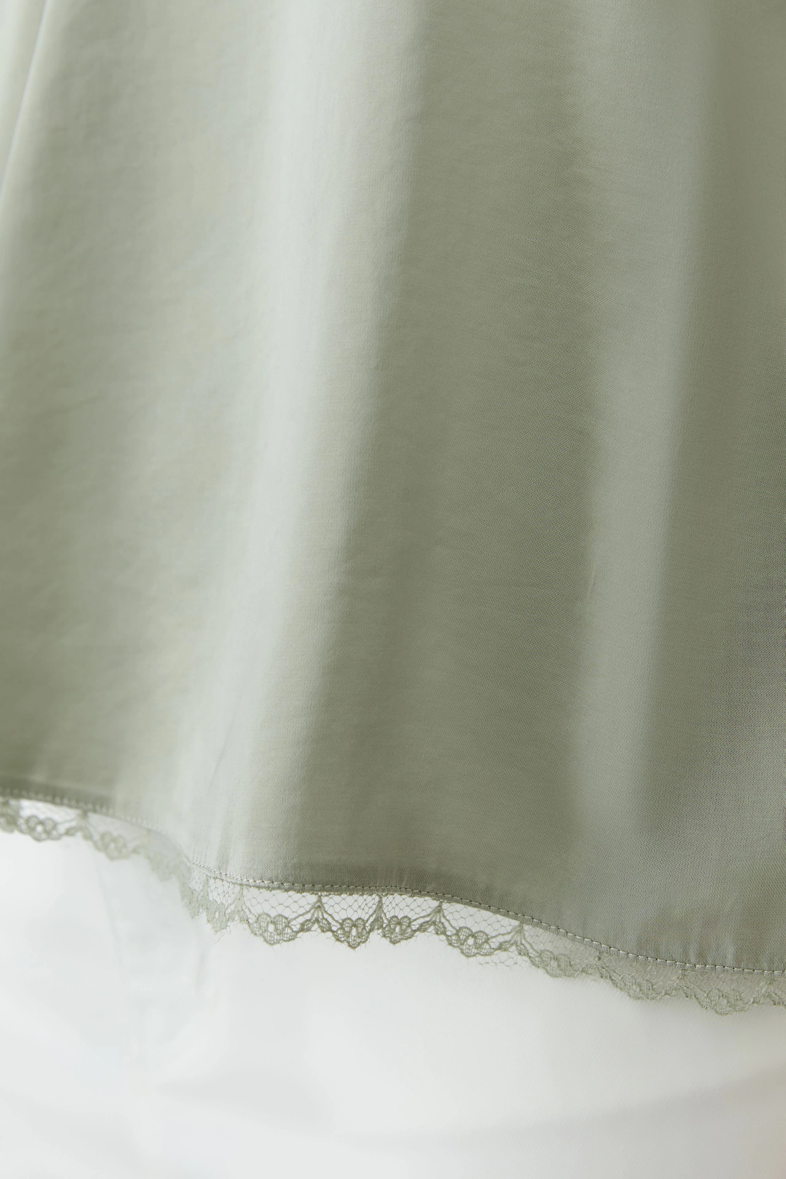 Casual women's top: Light green top with delicate lace hem, perfect for layering.