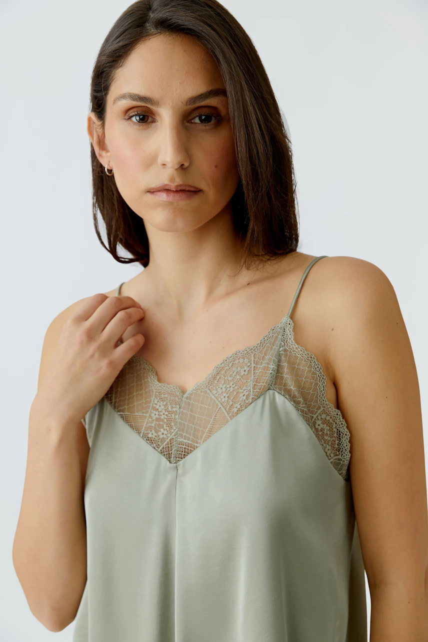 Casual women's top: Woman in a light green top with lace details, looking confidently at the camera.