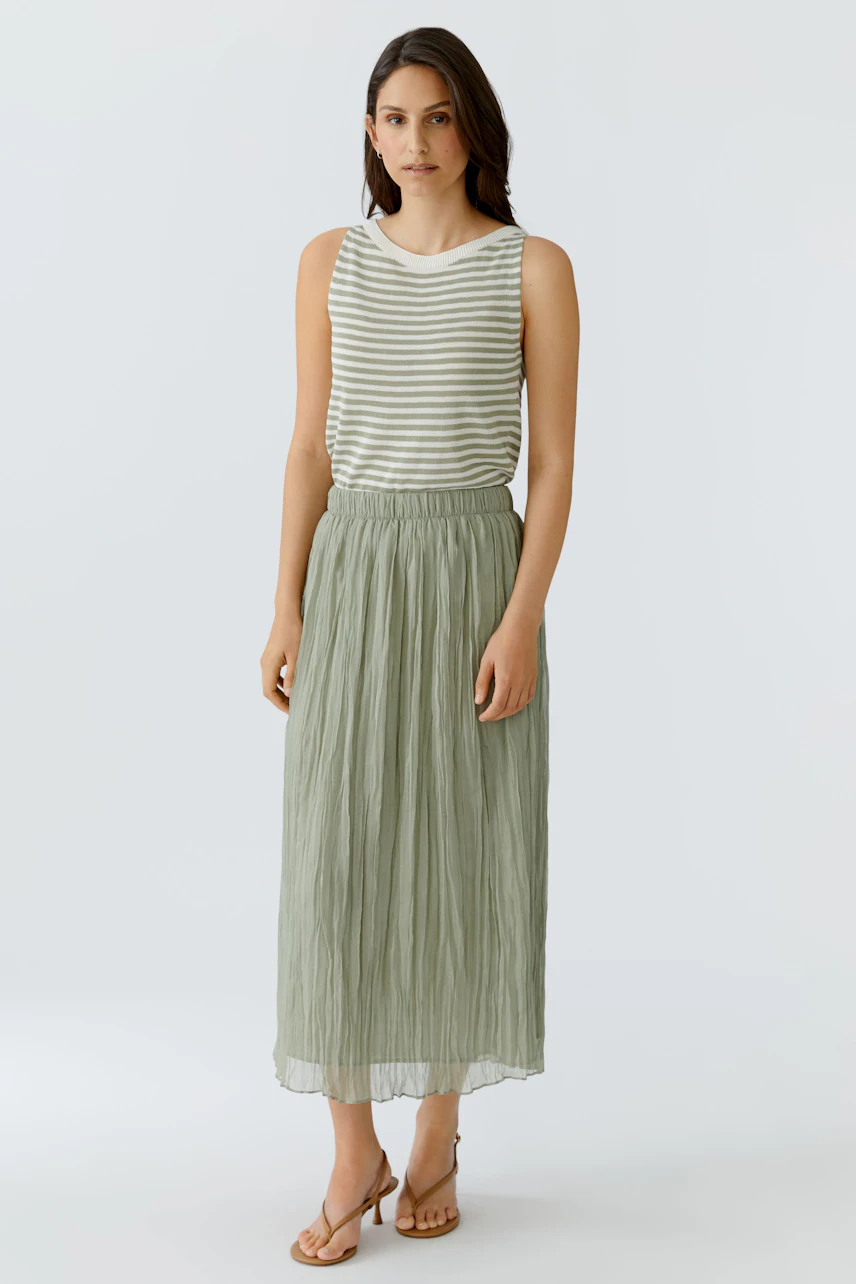 Woman in a striped top and green pleated skirt, standing confidently. Casual and stylish look.