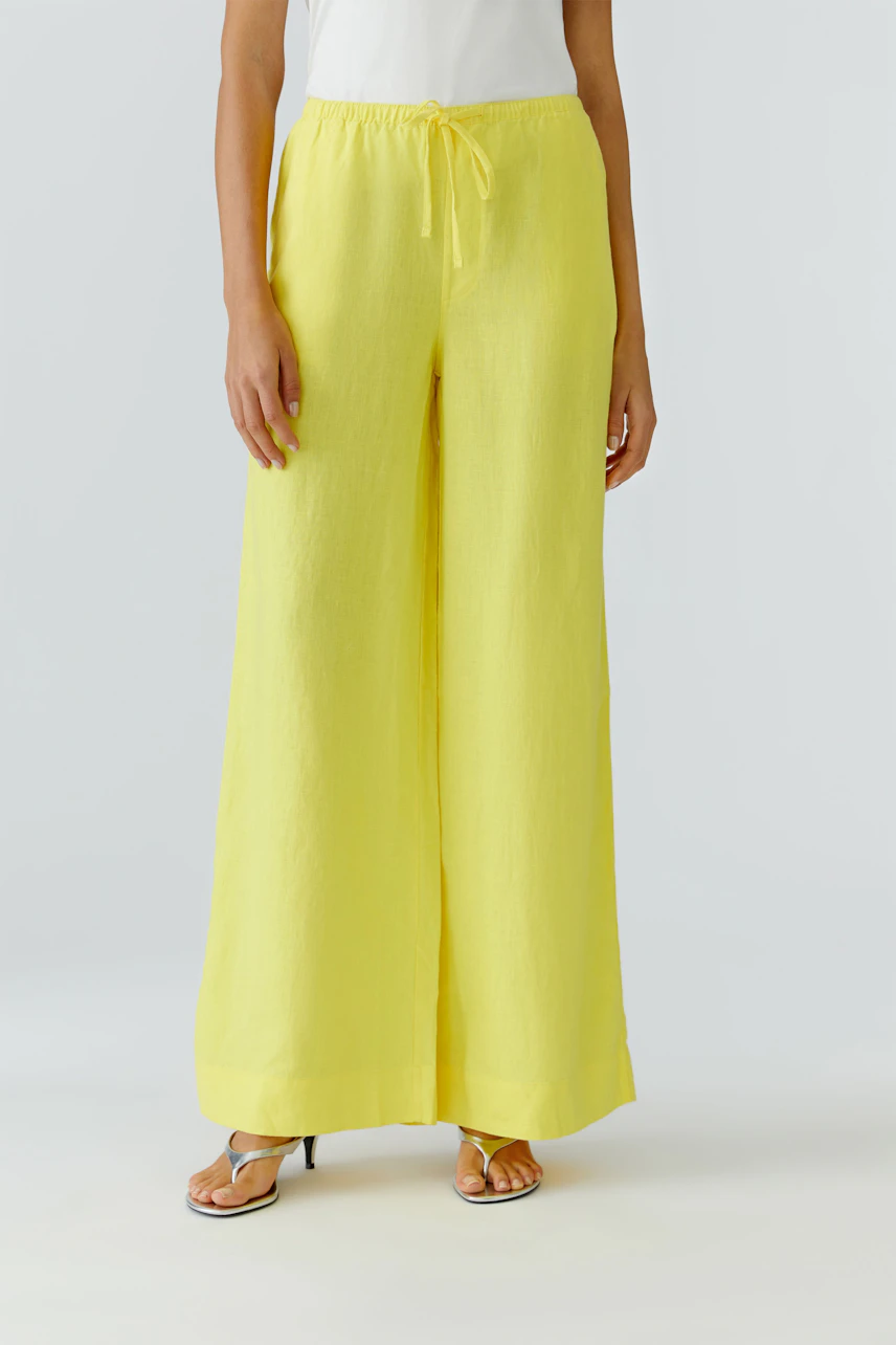 Woman in yellow Marlene pants, white top, and sandals. Relaxed fit with drawstring waist, perfect for casual wear.