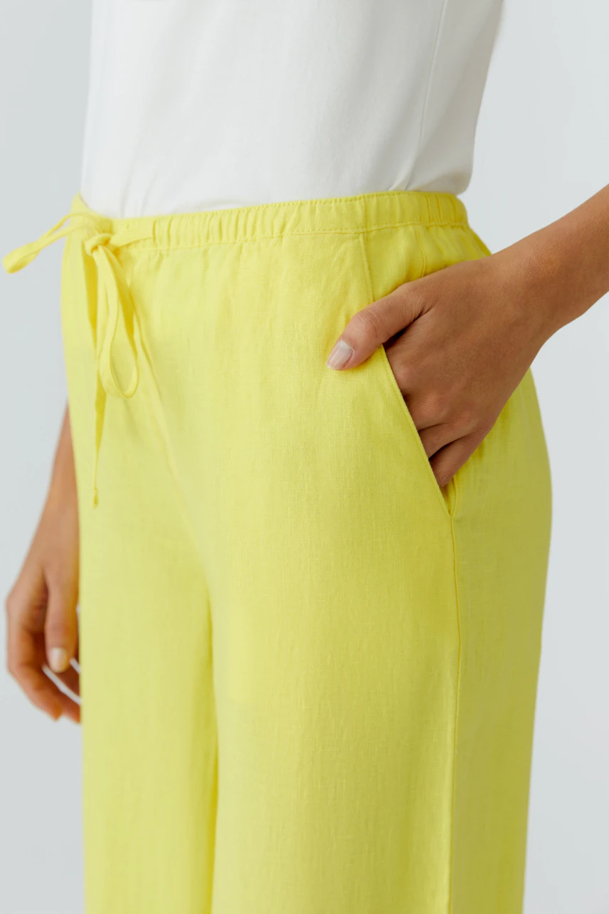 Woman in yellow Marlene trousers with a white top, hand in pocket, showcasing relaxed fit and style.