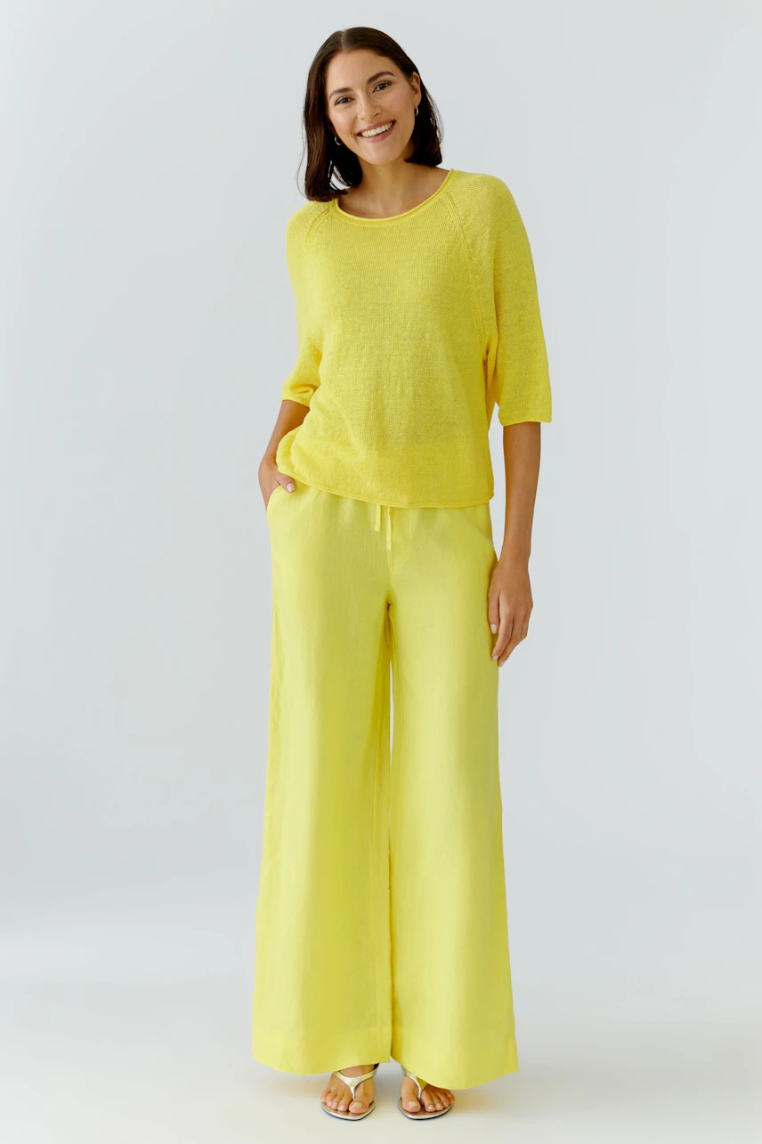 Woman in yellow Marlene pants and matching pullover, smiling confidently.