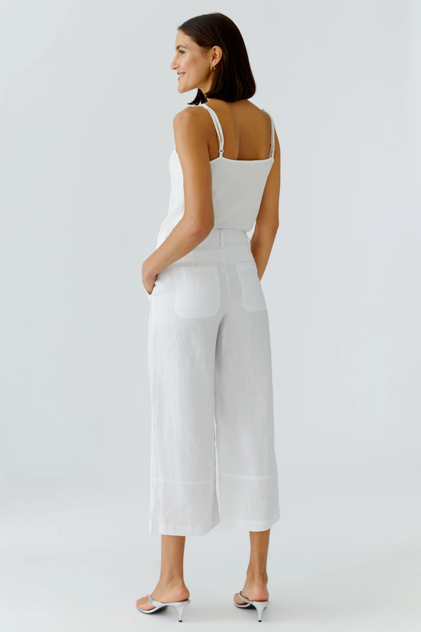 Weiße Damen-Hose: Frau in lockerer, weißer Hose und Top, seitlich stehend, mit entspanntem Ausdruck.