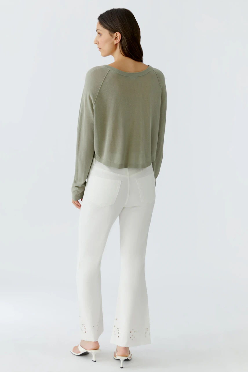 Lässige Strickjacke: Frau in olivgrüner Strickjacke und weißen Hosen, von hinten gesehen.