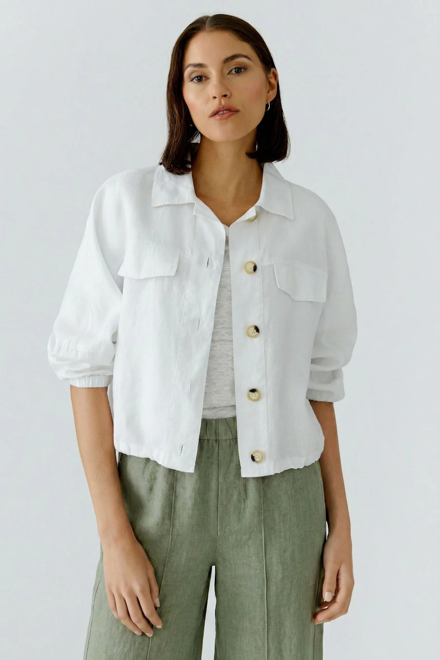Casual blouson: Woman in a white blouson with button-up front and brown shorts, standing confidently.